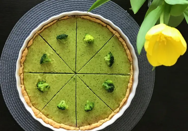 Zielona tarta z brokułami, pokrojona na 8 kawałków, ozdobiona różyczkami brokułów. Obok żółty tulipan.