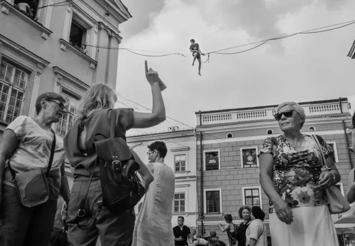 Uliczna fotografia: człowiek balansuje na linie, tłum obserwuje z dołu.