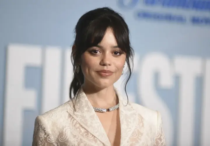 Jenna Ortega, uśmiechnięta, w białej koronkowej marynarce i efektownej biżuterii. Czy Jenna Ortega żyje? Tak, wygląda świetnie!