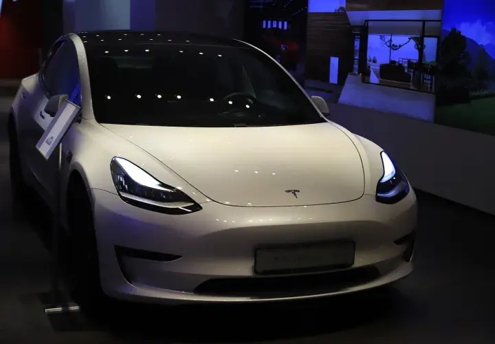 Biały samochód Tesla Model 3 z włączonymi światłami, prezentowany w salonie.