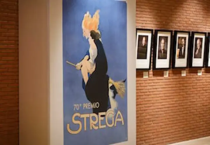 Un poster vintage celebra il 70° Premio Strega, con ritratti di autori appesi su una parete di mattoni.