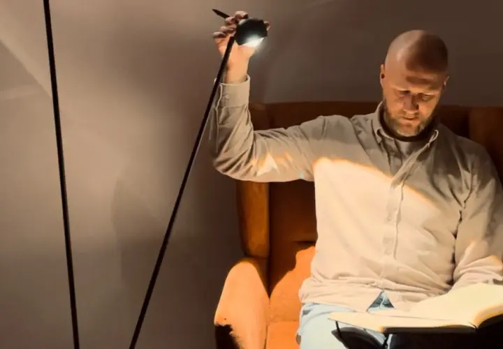 Hombre calvo sentado en sillón leyendo, iluminado por lámparas pie lectura.