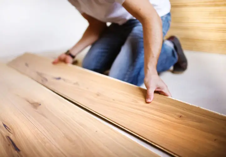 Uomo in ginocchio posa assi di legno per un pavimento con schema a spina di pesce.