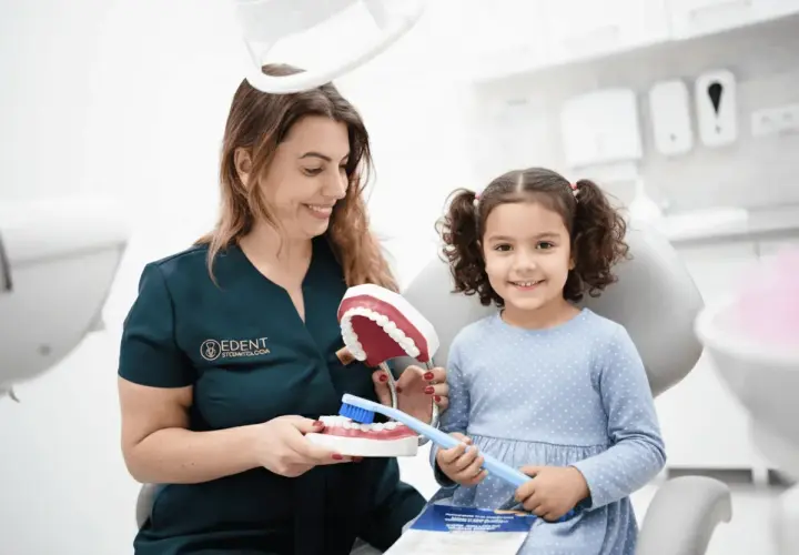 Dentystka uczy dziewczynkę higieny jamy ustnej, pokazując jak dbać o zęby, by miały mocny **hydroksyapatyt**.