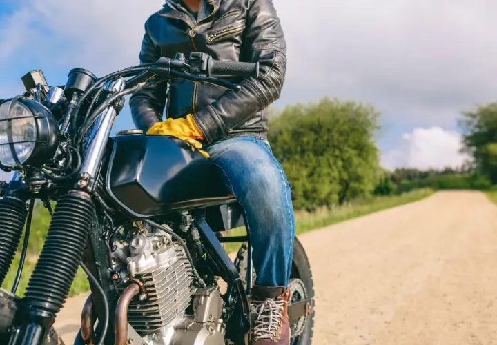 Motociclista con chaqueta de cuero y guantes amarillos, listo para la aventura. ¿Dyneema vs Kevlar? ¡La carretera espera!