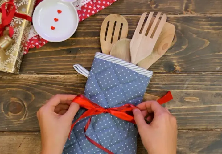 Idee regalo fai da te: un set di utensili da cucina in legno, avvolto in un guanto da forno a pois e legato con un nastro rosso.