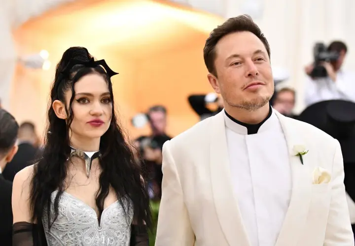 Grimes i Elon Musk na czerwonym dywanie. Ona w srebrnej kreacji z nietypowym naszyjnikiem, on w białej marynarce.