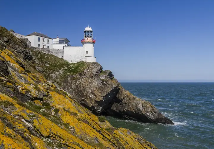 Biała latarnia morska na skalistym klifie nad morzem, Irlandia.