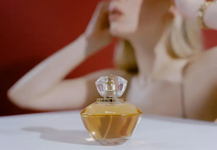 Elegancka buteleczka perfum z płynem o barwie **citral** na białym tle, w tle niewyraźna sylwetka kobiety.