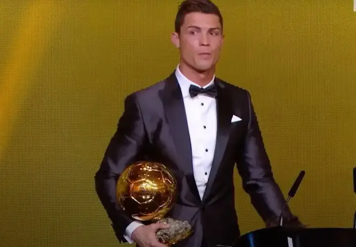 Cristiano Ronaldo w garniturze trzyma złotą piłkę. Ile złotych piłek ma Ronaldo? To pytanie zadaje sobie wielu fanów.