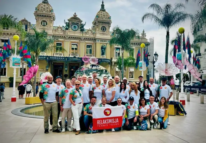 Grupa turystów z flagą "RelaksMisja Tennis Tours" przed kasynem w Monte Carlo. Wszyscy ubrani w koszulki z motywem kwiatowym.