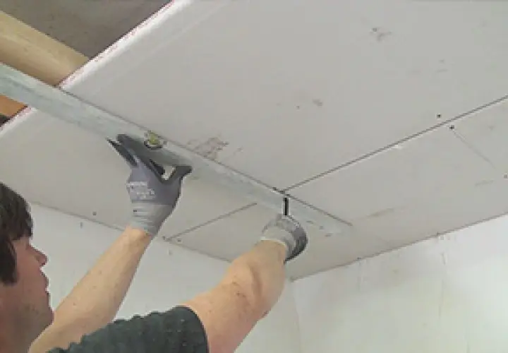 Handwerker bearbeitet Decke mit Rigipsplatten. Die Dicke der Platten ist entscheidend für Stabilität und Dämmung.