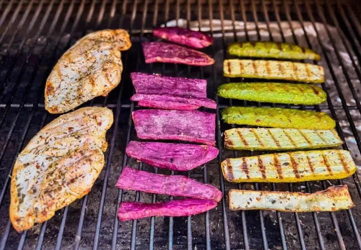 Deux blancs de poulet au barbecue, accompagnés de tranches de patate douce violette et de courgettes grillées, sur une grille.