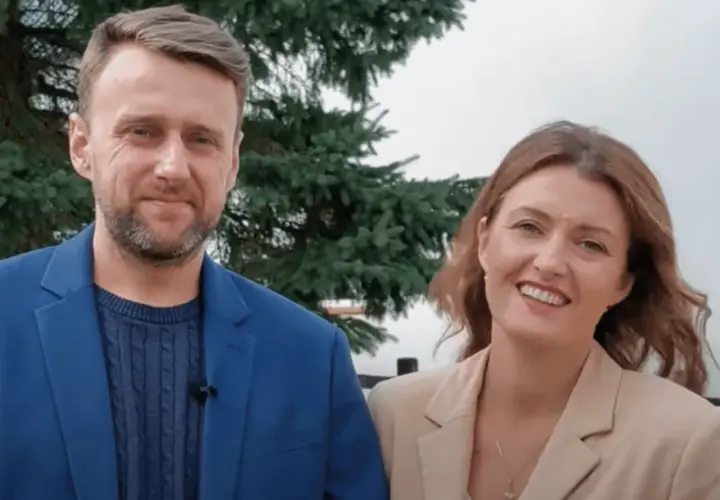 Uśmiechnięta para, on w niebieskiej marynarce, ona – żona z Ukrainy – w beżowej.
