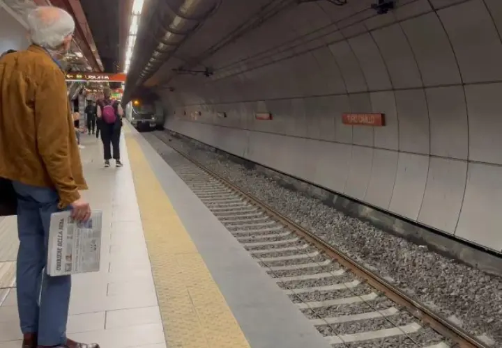 Uomo attende treno alla stazione Valle Aurelia Termini, con giornale in mano.
