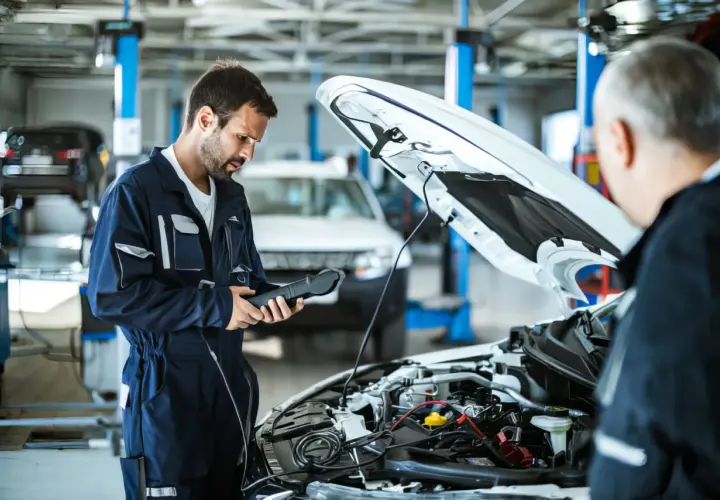 Mecánico revisa el motor de un coche diesel con un escáner. El capó está abierto, mostrando el complejo sistema.