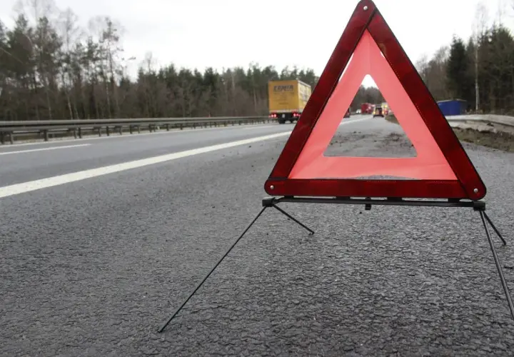 Trójkąt ostrzegawczy na poboczu drogi, zapowiadający 3 mieczy pozytywnie. W tle ciężarówka i inne pojazdy.