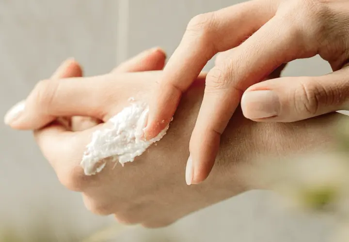 Delikatny peeling do rąk rozprowadzany palcami, z widocznym zadbanym paznokciem.
