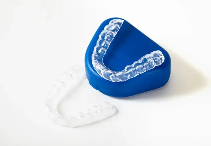 Alineadores transparentes para ortodoncia, uno sobre un estuche azul y otro al lado. ¿Cuánto cuesta el invisible line?
