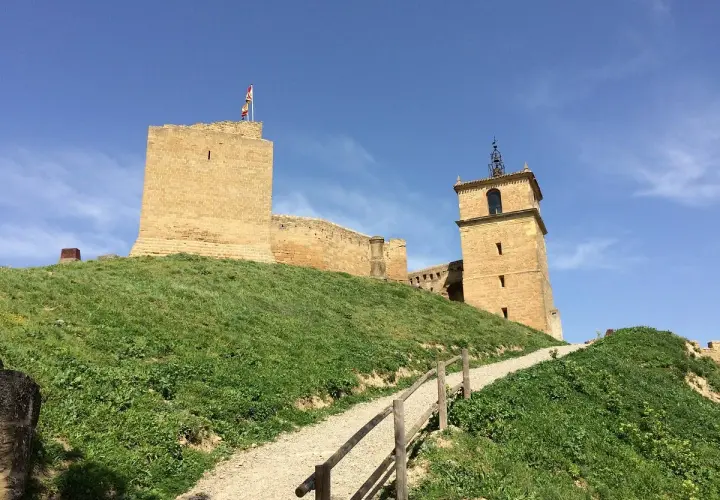 El castillo de San Vicente de la Barquera se alza majestuoso sobre una colina verde, con su torre y murallas de piedra bajo un cielo azul.