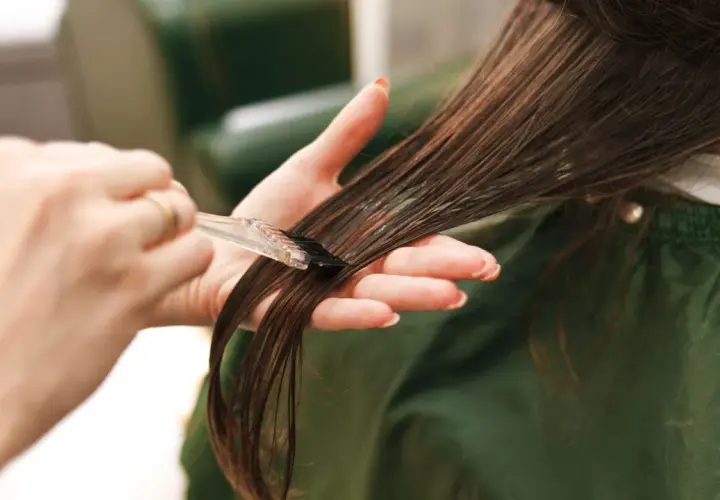 Manos aplicando tinte en el cabello. Cuidado con la alergia al tinte de pelo.