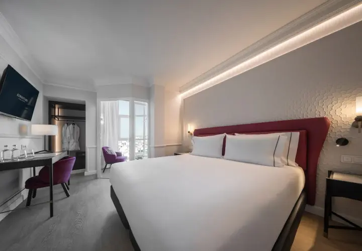 Habitación moderna y luminosa en el hotel San Antón Granada. Cama doble con cabecero rojo, escritorio, sillón morado y vistas.