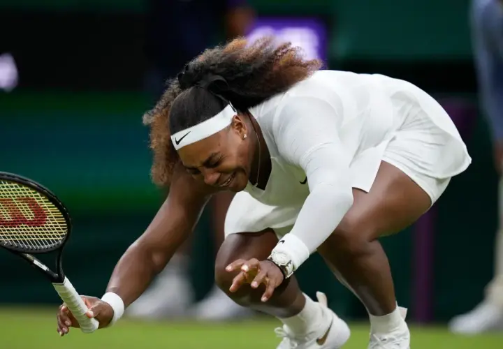 Serena Williams upada na kort podczas meczu tenisa w Wimbledonie, trzymając rakietę.