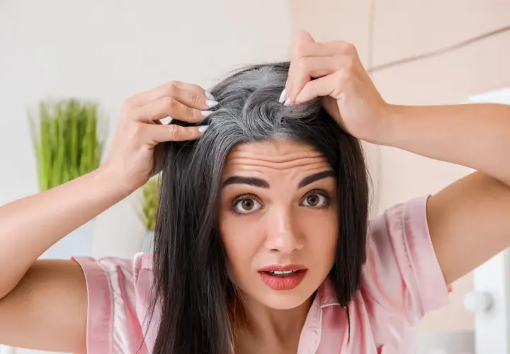 Mujer preocupada por sus canas, buscando una solución natural con mechas sin amoniaco.