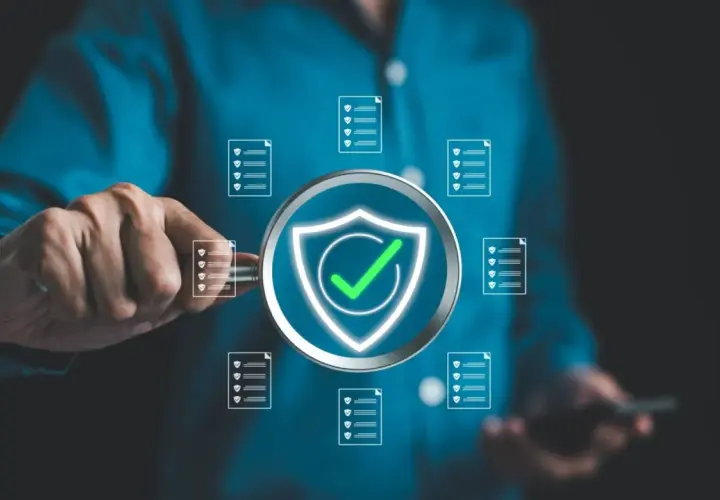 Un uomo esamina documenti con una lente d'ingrandimento, evidenziando un simbolo di scudo con un segno di spunta verde, a simboleggiare la sicurezza e l'efficienza nella sanità pubblica.