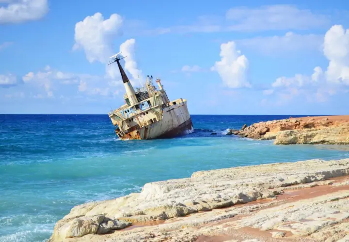 Wraki statków na pafos plażach. Zardzewiały statek osiadł na mieliźnie przy skalistym wybrzeżu, woda jest turkusowa, a niebo błękitne z białymi chmurami.