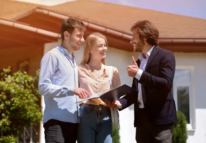 Un couple discute avec un agent immobilier devant une maison, signe d'une vente en cascade réussie.