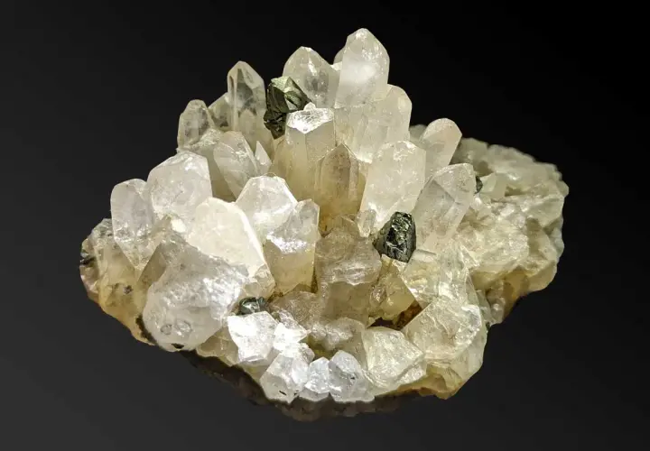 Ein Cluster aus klaren, facettierten Quarz-Kristallen mit dunklen Einschlüssen. Was ist Quarz? Ein faszinierendes Mineral!
