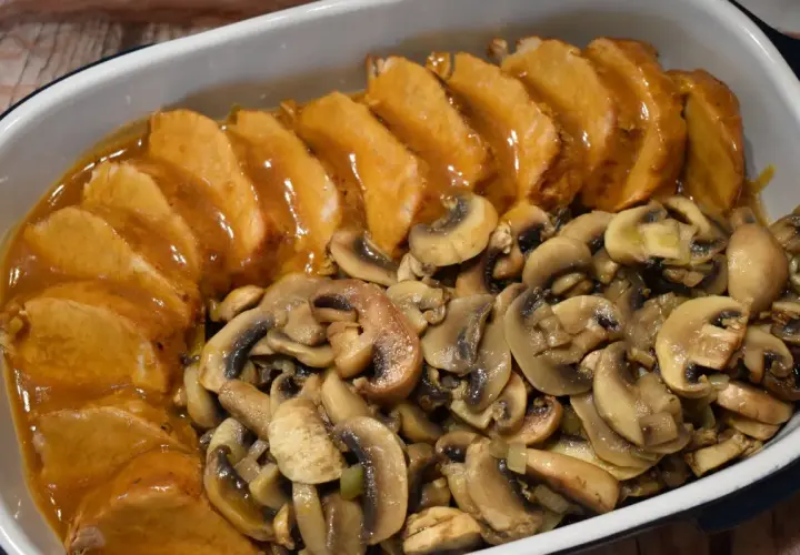 Pyszny schab z pieczarkami w sosie, podany w naczyniu żaroodpornym. Aromatyczne pieczarki idealnie komponują się z soczystym mięsem.