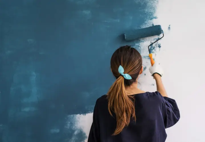 Mujer aplicando imprimación azul en pared con rodillo. Aprende como dar imprimación en paredes para un acabado perfecto.