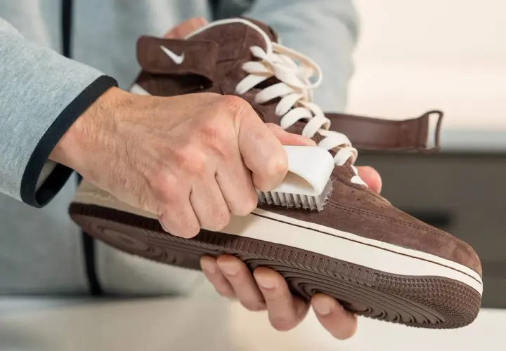 Man limpiando zapatillas de gamuza marrón con un cepillo blanco. Aprende como quitar cera de los zapatos de piel.