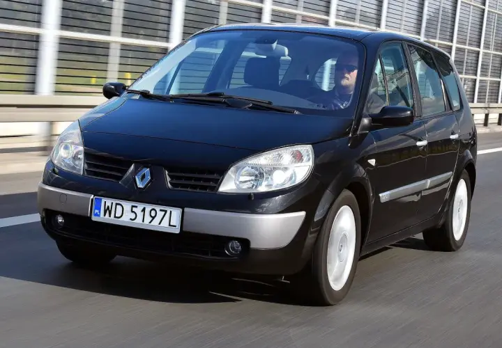 Czarny Renault Scenic 2 jedzie po drodze. Kierowca w okularach przeciwsłonecznych prowadzi auto.