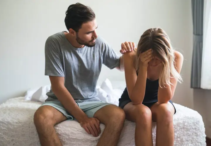Hombre consuela a mujer afligida en la cama. ¿Qué significa soñar que tu pareja te es infiel?