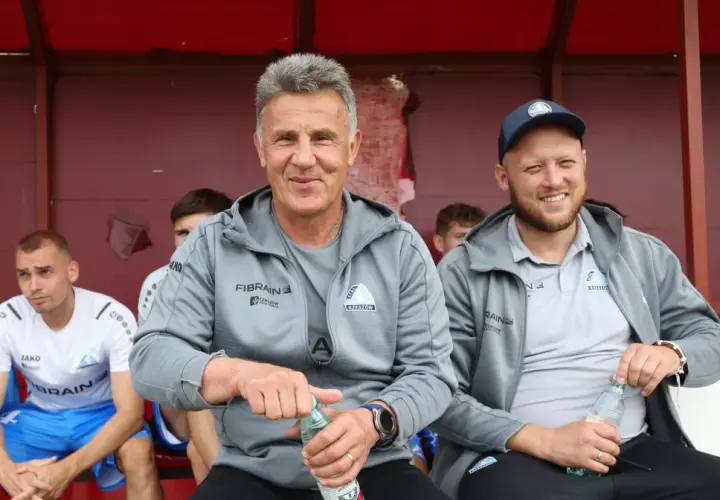 Marek Zub, trener Stali Rzeszów, z uśmiechem na twarzy, siedzi na ławce z butelką wody.