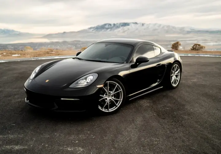 Czarne Porsche Cayman na tle gór i jeziora. Zastanawiasz się, ile kosztuje Porsche?