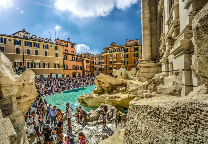 Fontana di Trevi, un vero gioiello tra gli imperdibili di Roma, affollata di turisti che ammirano la sua maestosità sotto un cielo azzurro.