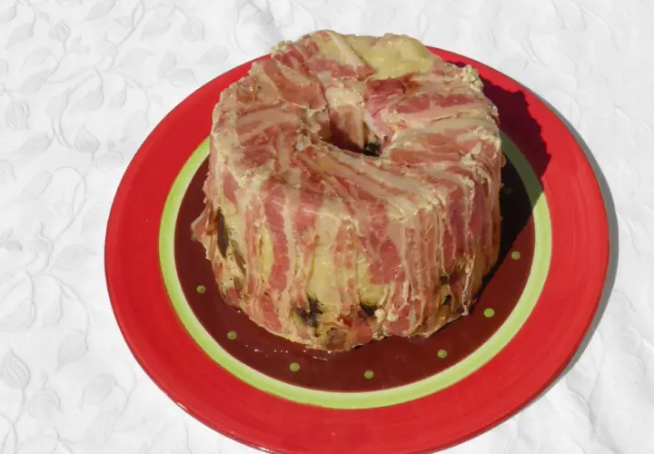 Un pâté en croûte de lard, une recette qui ne demande pas de farcement. Il est servi sur une assiette rouge décorée.