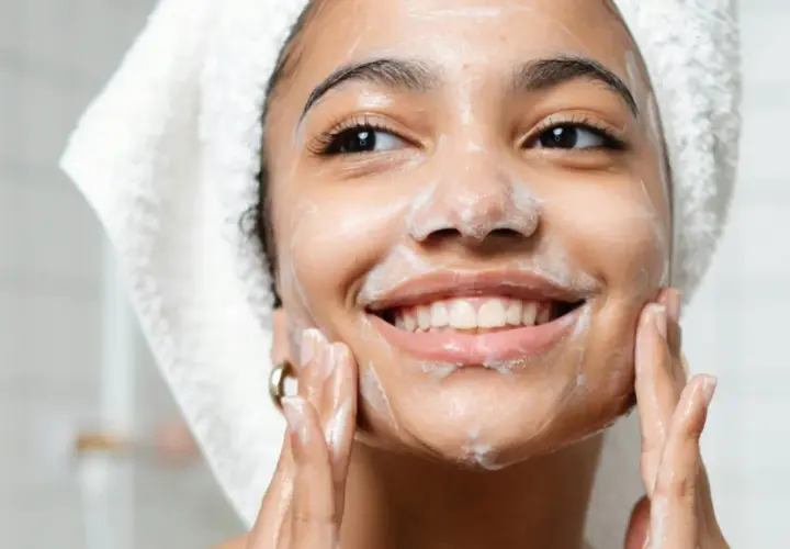 Mujer sonriente con espuma en el rostro, disfrutando de su rutina de doble limpieza facial.