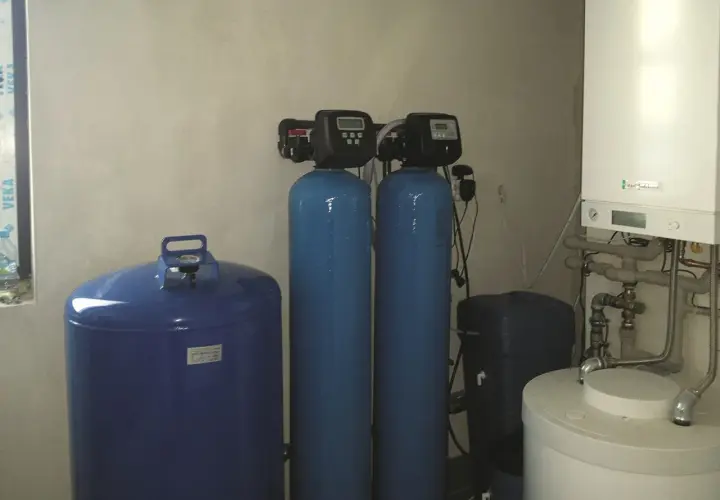 System do uzdatniania wody: niebieski zbiornik, dwa pionowe cylindry z panelami sterowania i biały bojler.