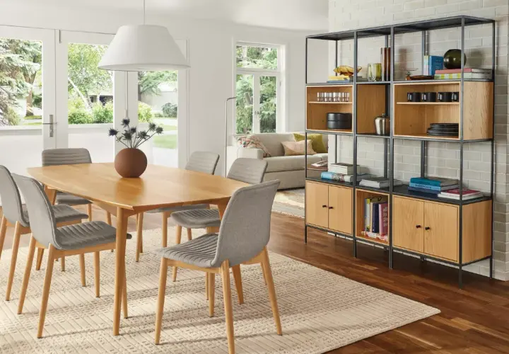 Open living and dining room ideas: a light wood table with grey chairs, a modern shelving unit, and a sofa visible through French doors.