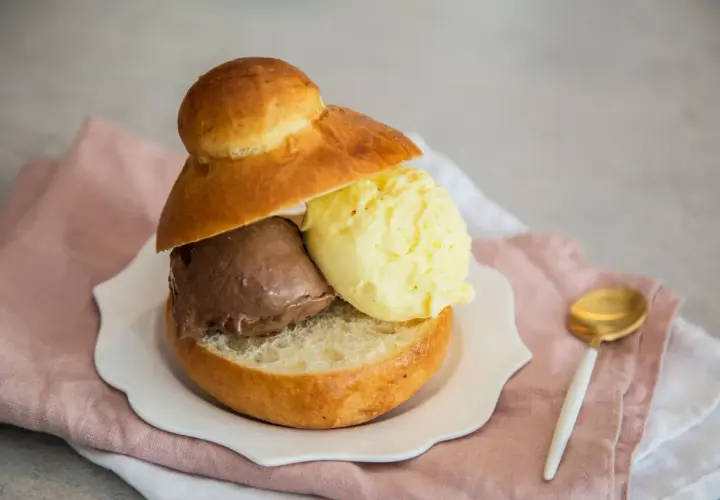 Pyszne lody w bułce: czekoladowe i waniliowe, podane na talerzyku z różową serwetką.