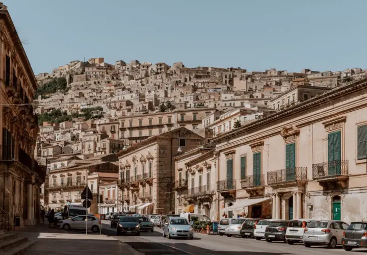 Cars navigate a steep, narrow street in a Sicilian town. Driving here might be challenging, but the views are worth it!