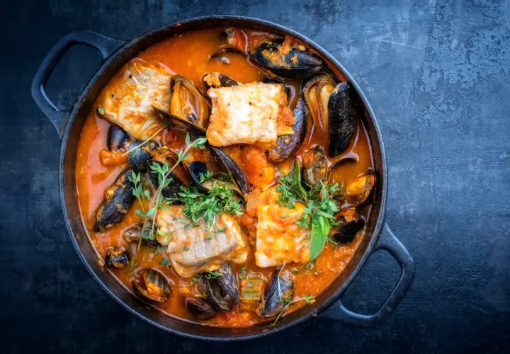 Una ricca zuppa di pesce in una pentola di ghisa, con pezzi di pesce bianco, cozze e erbe aromatiche fresche.