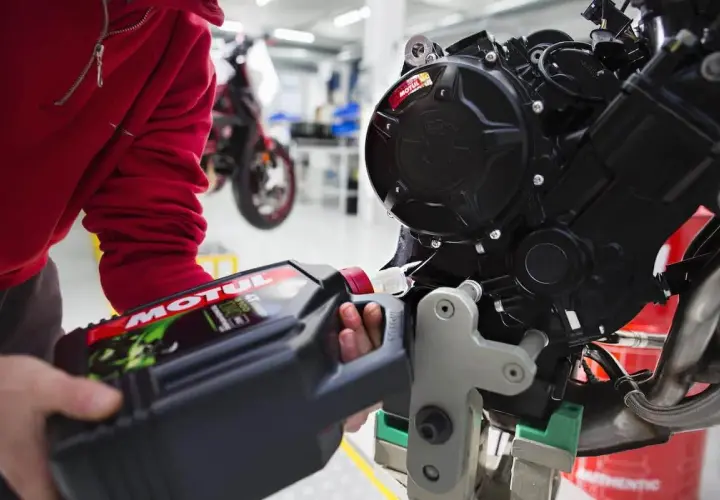 Osoba w czerwonej bluzie nalewa olej Motul do silnika motocykla. Pamiętaj, co ile wymieniać olej w motocyklu, by zapewnić mu długą żywotność.