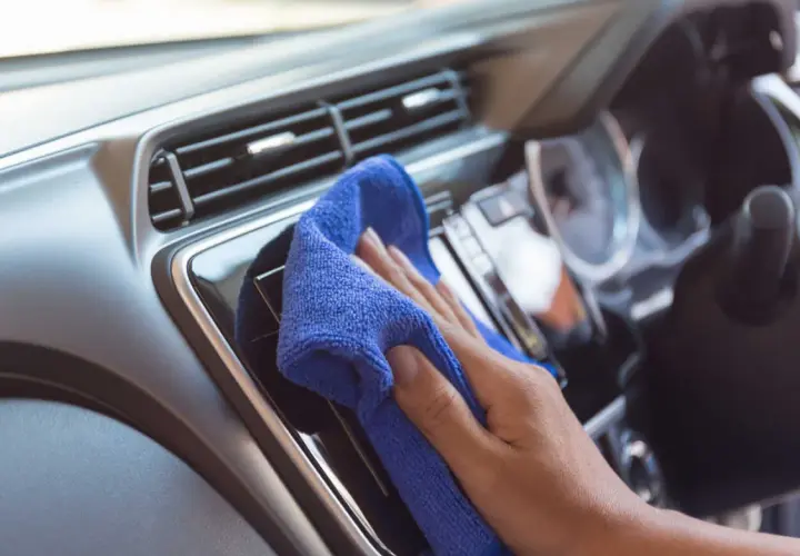 Mano che pulisce il cruscotto dell'auto con un panno blu. Una guida su come pulire il cruscotto della macchina per mantenerlo splendente.