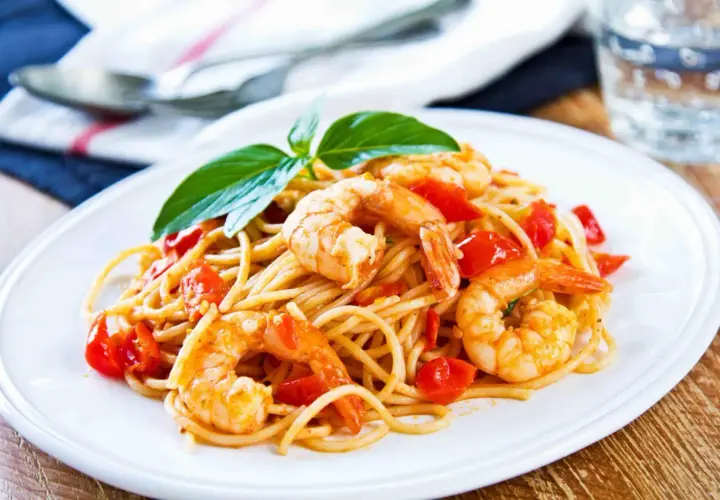 Un piatto invitante di pasta con gamberetti e pomodorini, guarnito con basilico fresco.